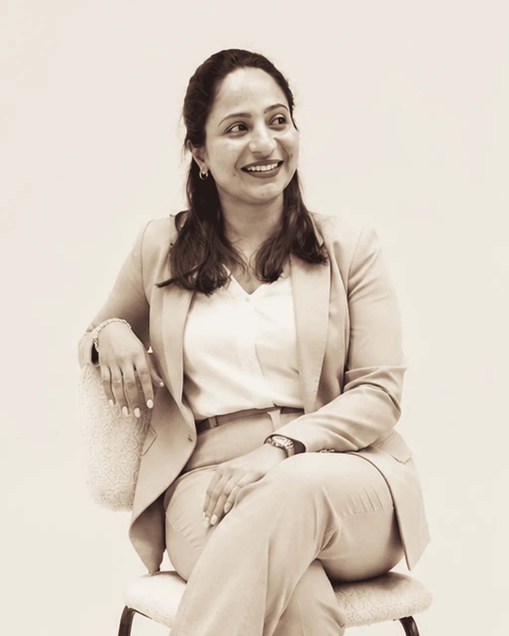 Mubeena, seated, smiling, in a sand-coloured suit.